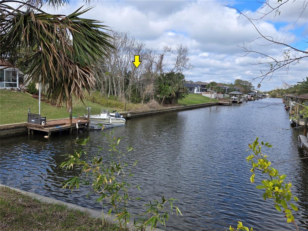A canal view showing a boat docked at a wooden pier beside a wooded lot — 25 CHRISTOPHER COURT N, PALM COAST, FL