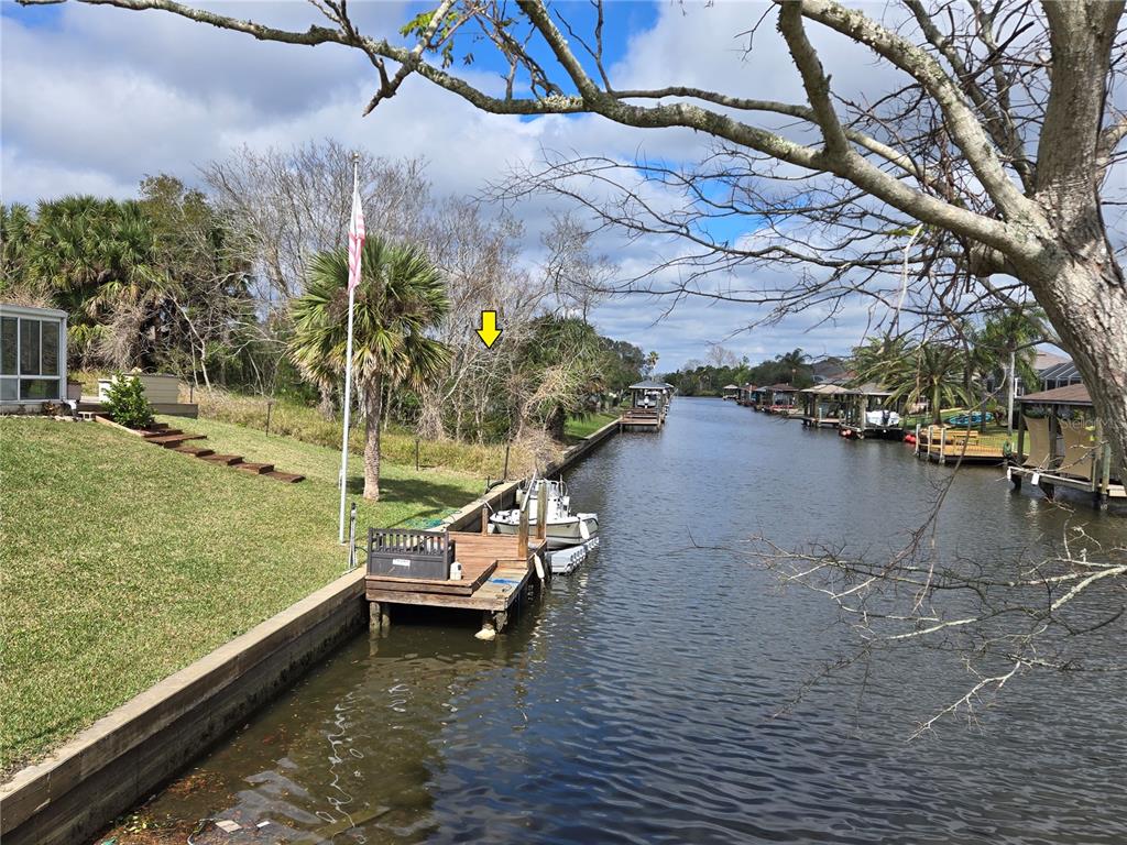 A canal view showing a wooden dock, a boat, and a grassy backyard with trees — 25 CHRISTOPHER COURT N, PALM COAST, FL