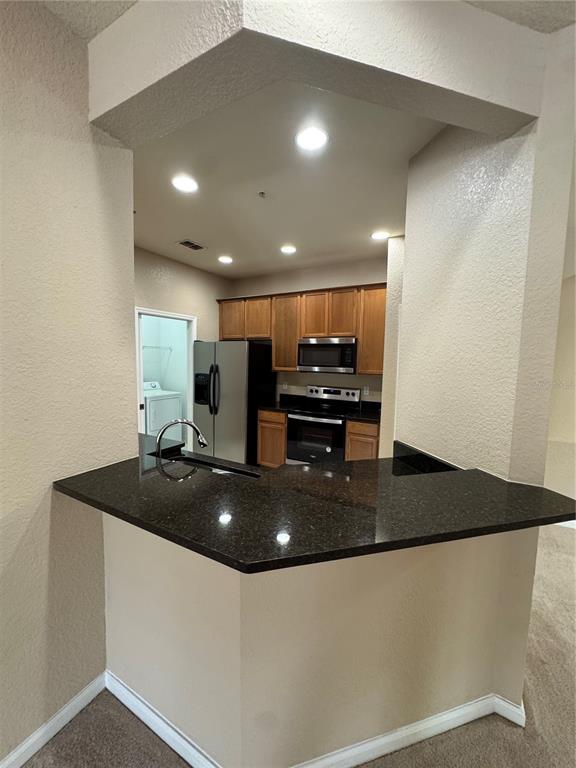 A kitchen features dark granite countertops, wood cabinets, and stainless steel appliances — 3331 WHITESTONE CIRCLE UNIT 101, KISSIMMEE, FL