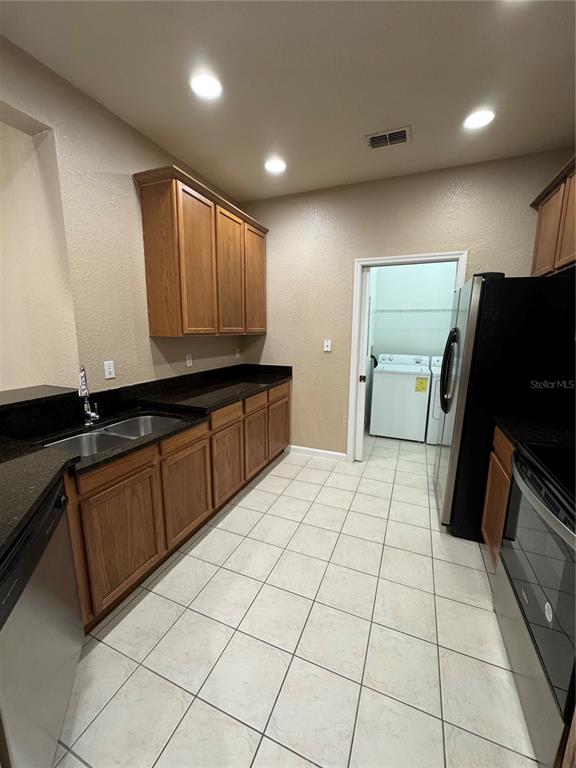 A kitchen with wood cabinets, dark countertops, tile flooring, and an adjacent laundry room — 3331 WHITESTONE CIRCLE UNIT 101, KISSIMMEE, FL