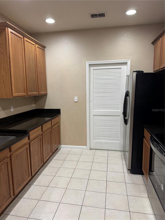 A kitchen features wood cabinets, dark countertops, a white louvered door, and tiled flooring — 3331 WHITESTONE CIRCLE UNIT 101, KISSIMMEE, FL