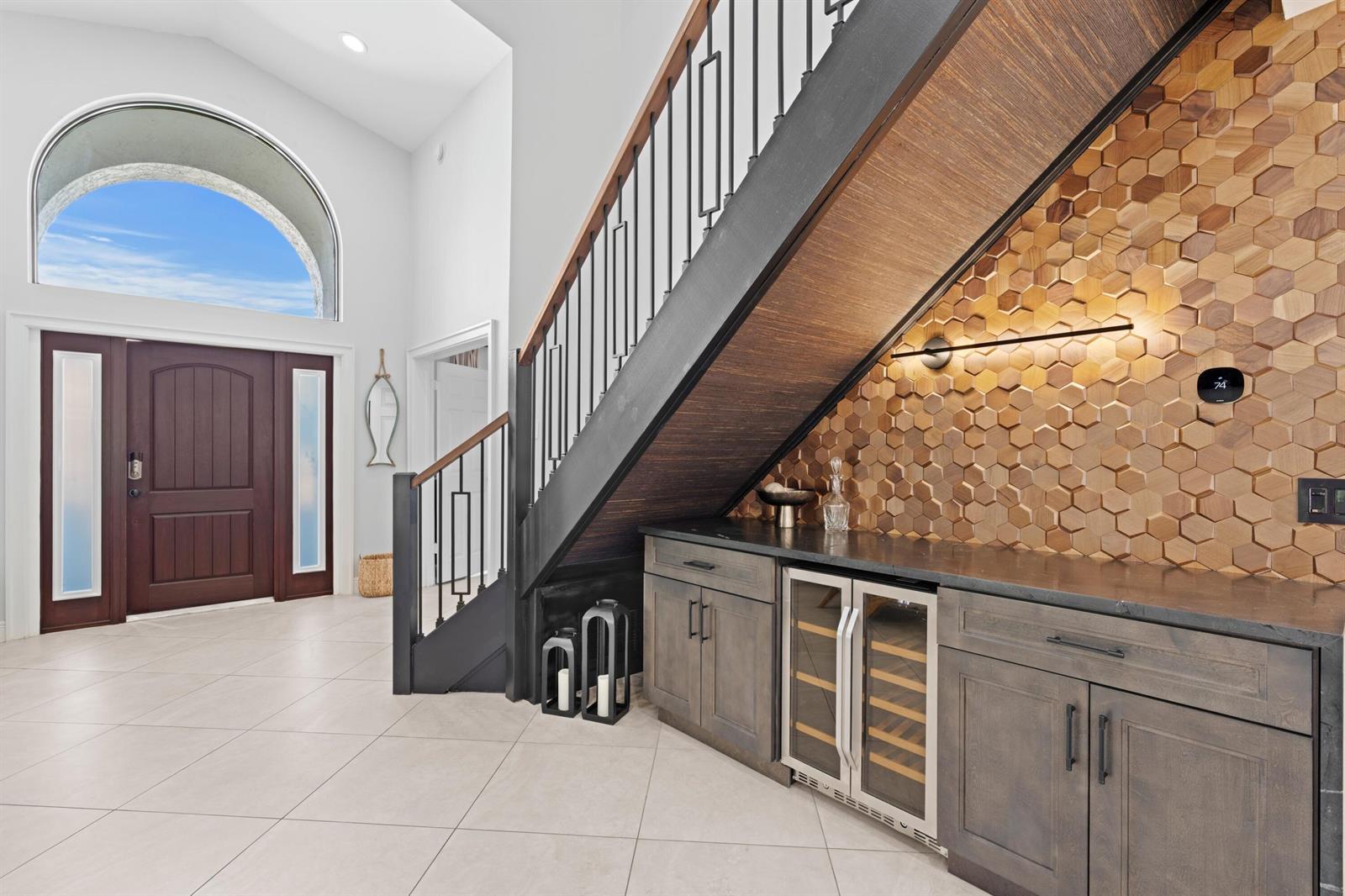 A foyer features a staircase with a built-in bar, wood-tiled wall, and tile flooring — 1050 Brooks Lane, Delray Beach FL 33483, DELRAY BEACH, FL