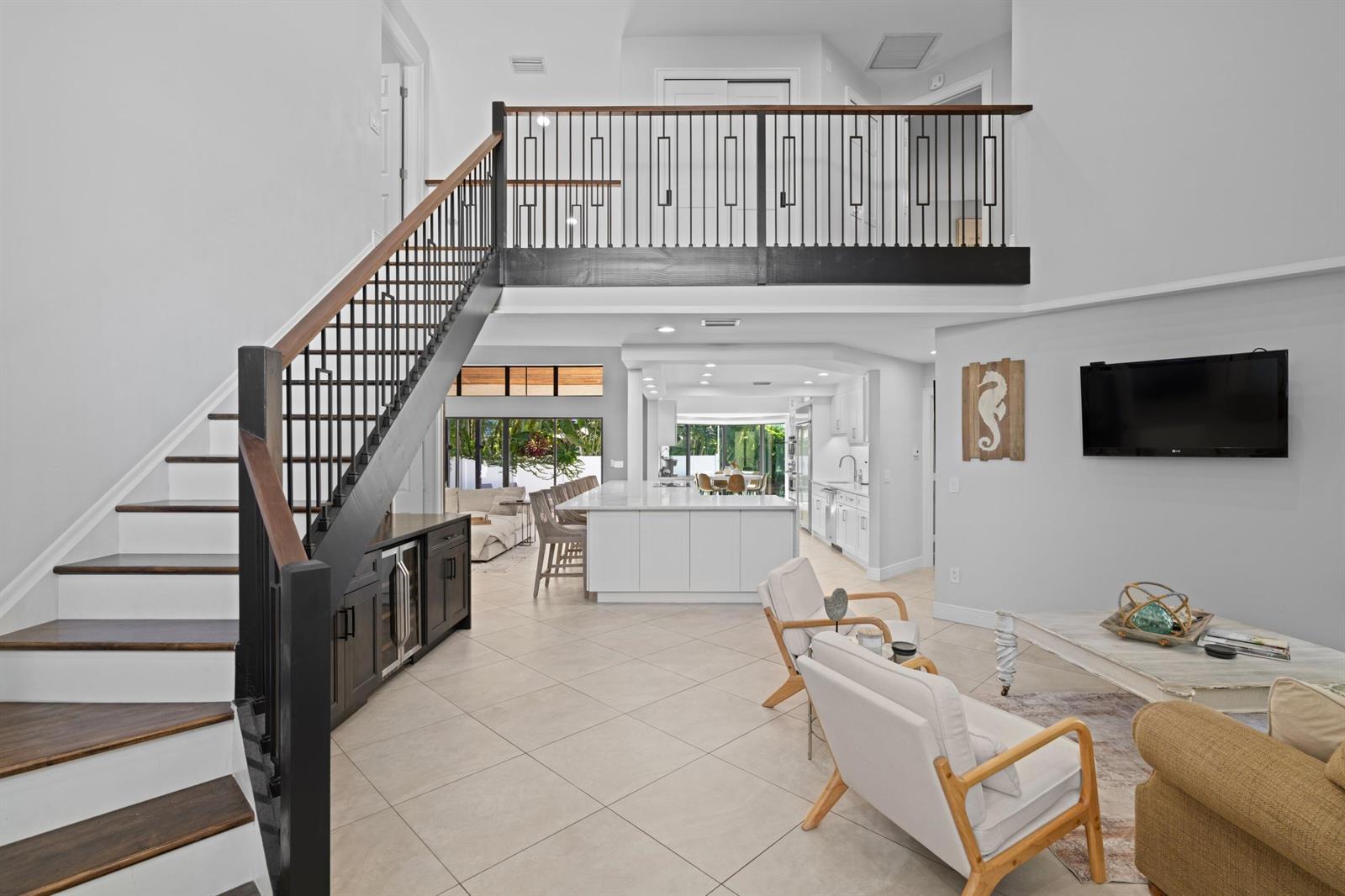 A modern living room and kitchen area features a staircase with black railings and tile flooring — 1050 Brooks Lane, Delray Beach FL 33483, DELRAY BEACH, FL