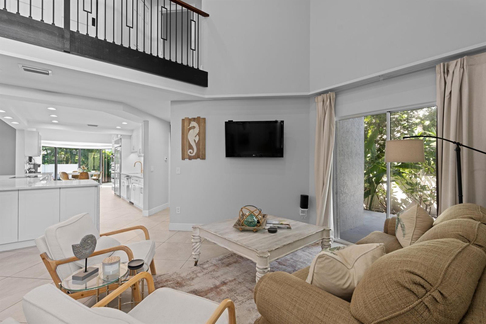 A living room with a high ceiling, a mounted television, and a view of the kitchen — 1050 Brooks Lane, Delray Beach FL 33483, DELRAY BEACH, FL