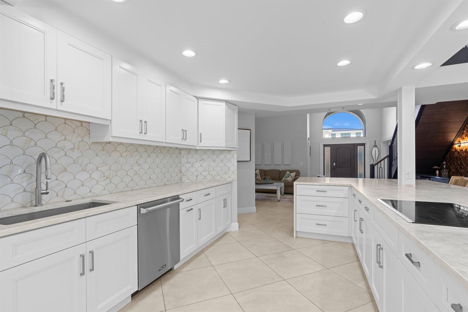 A white kitchen features a scalloped tile backsplash, stainless steel appliances, and light stone countertops — 1050 Brooks Lane, Delray Beach FL 33483, DELRAY BEACH, FL