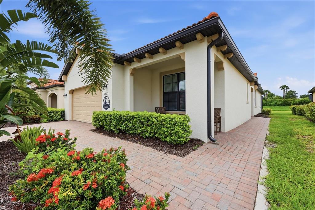 A single-story house with a beige stucco exterior, a brick paver walkway, and a garage — 24173 SPARTINA DRIVE, VENICE, FL