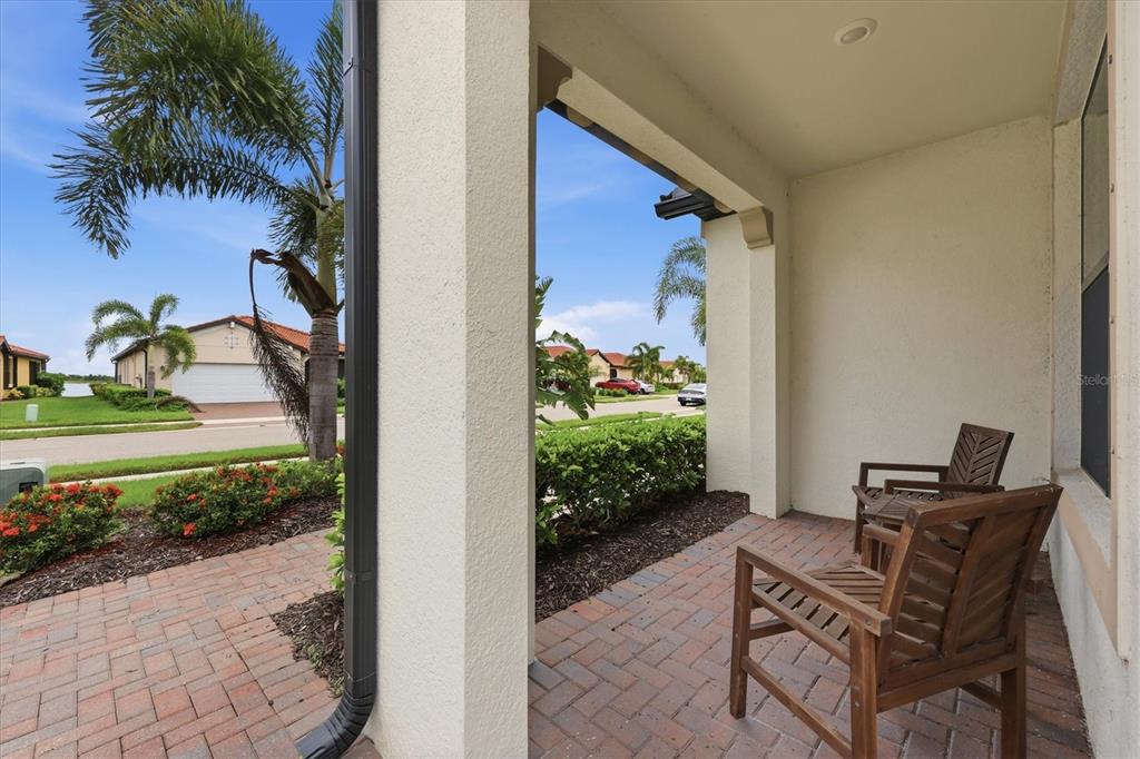 A covered brick patio features two wooden chairs and a view of a suburban street — 24173 SPARTINA DRIVE, VENICE, FL