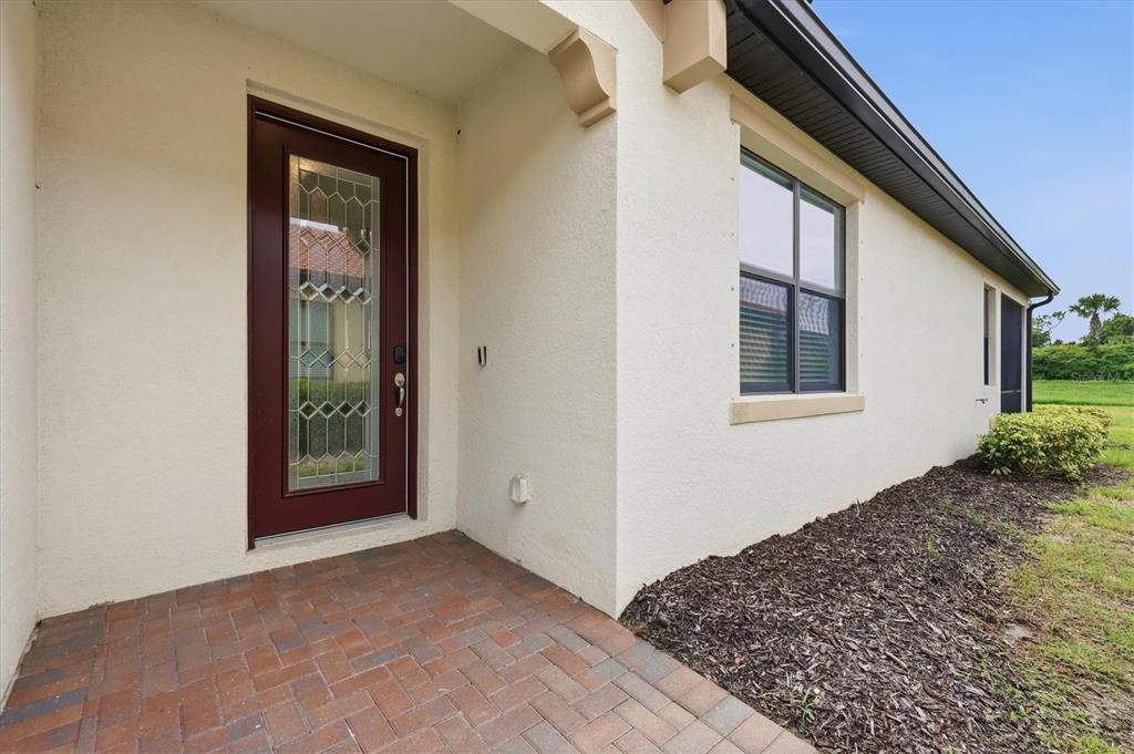 A brick-paved entryway leads to a front door with a decorative glass panel — 24173 SPARTINA DRIVE, VENICE, FL