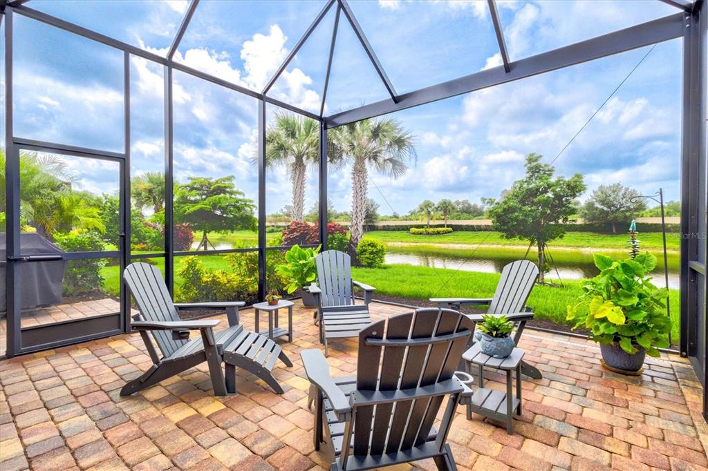 A screened-in brick patio features Adirondack chairs overlooking a pond and green landscape — 13179 BORREGO STREET, VENICE, FL