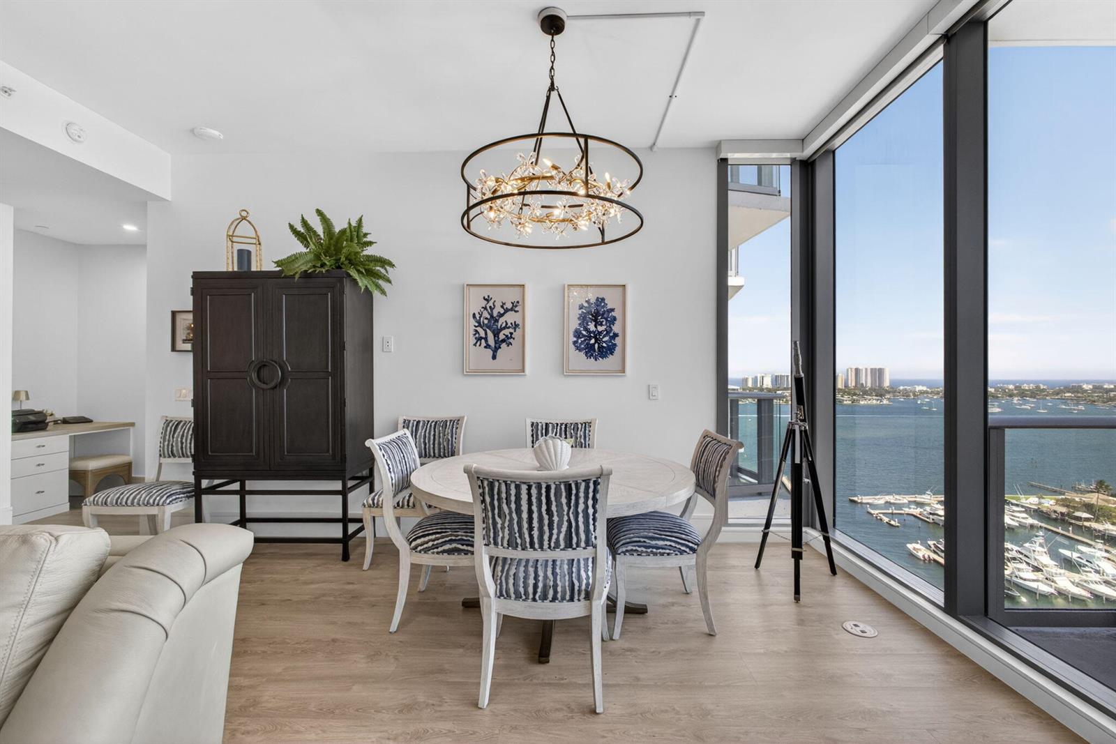 A dining area features a round table, striped chairs, a chandelier, and floor-to-ceiling windows — 220 Lake Shore Drive # 1907, West Palm Beach FL 33403, WEST PALM BEACH, FL