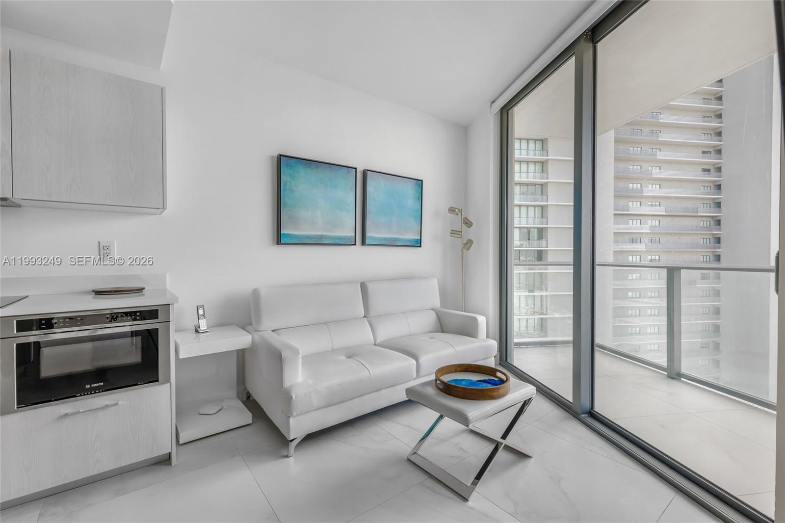 A modern living area features a white sofa, small table, and balcony with city views — 501 NE 31 St # 2407, Miami FL 33137, MIAMI, FL