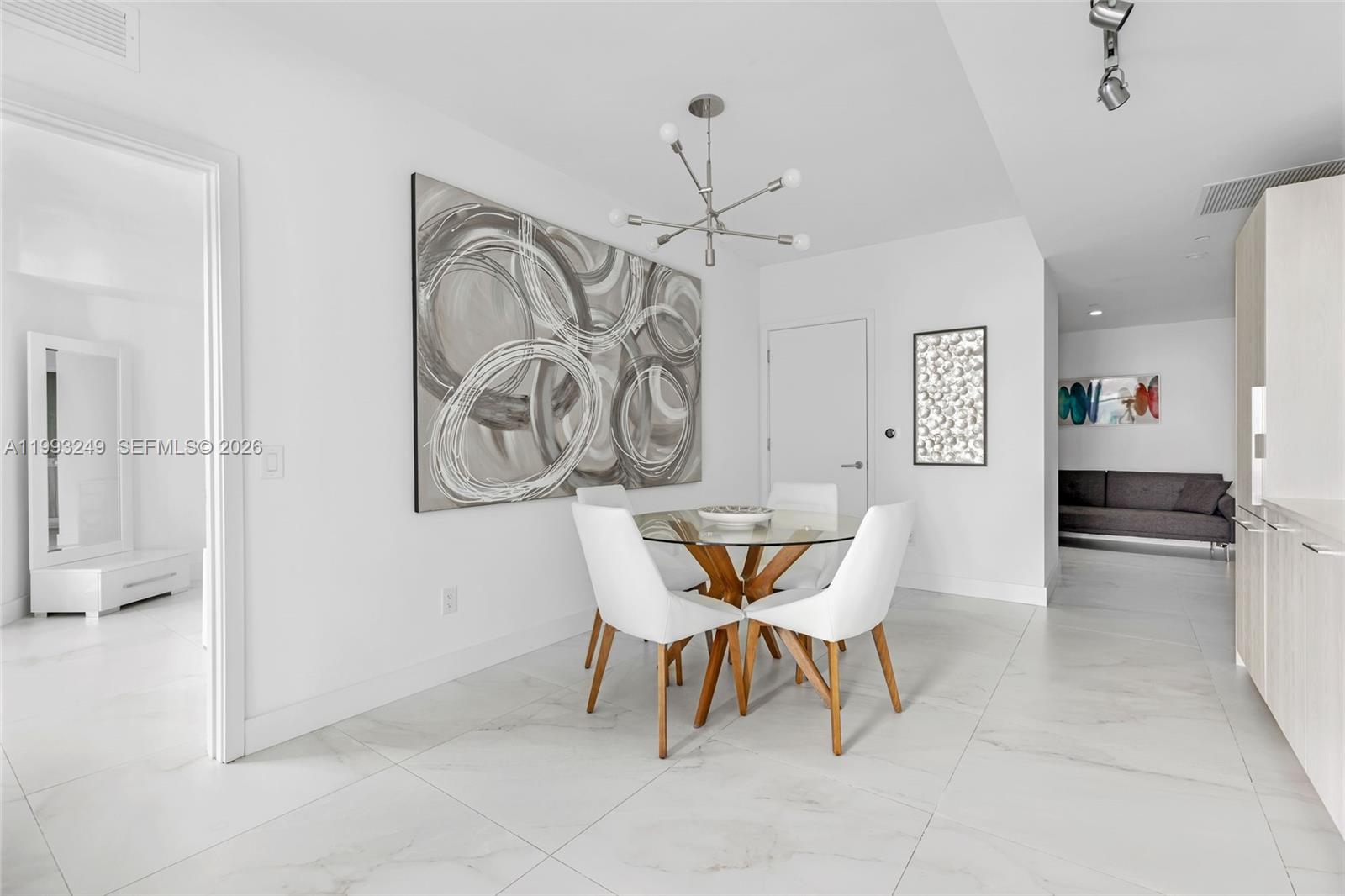 A dining area features a glass-topped table, four white chairs, and large abstract wall art — 501 NE 31 St # 2407, Miami FL 33137, MIAMI, FL