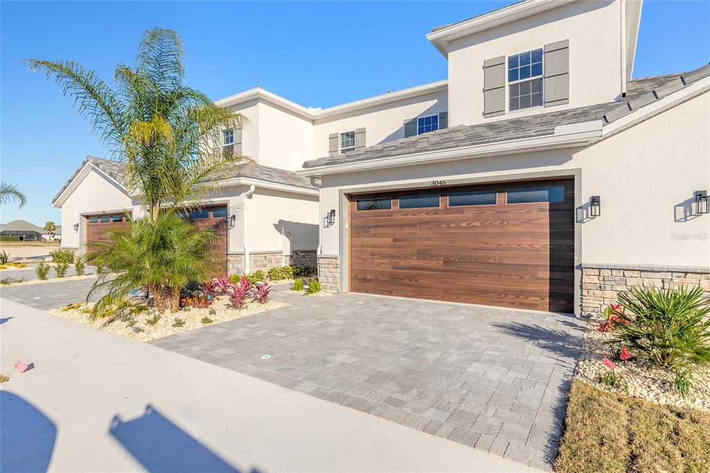 A two-story townhouse exterior features a wood-look garage door, stone accents, and a paved driveway — 3057 ISLES WAY, NEW SMYRNA BEACH, FL