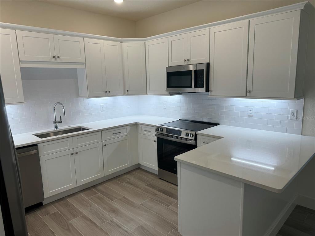 A kitchen features white cabinets, stainless steel appliances, white countertops, and a subway tile backsplash — 3057 ISLES WAY, NEW SMYRNA BEACH, FL