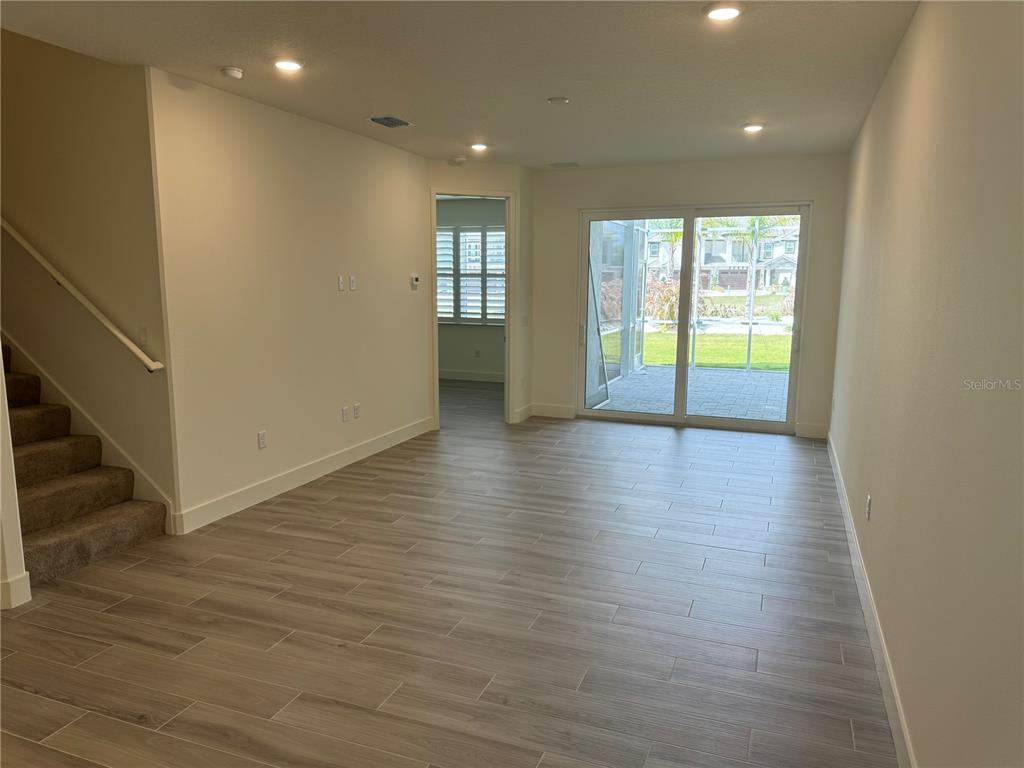 An open living area features light wood-look tile flooring, a staircase, and sliding glass doors — 3057 ISLES WAY, NEW SMYRNA BEACH, FL