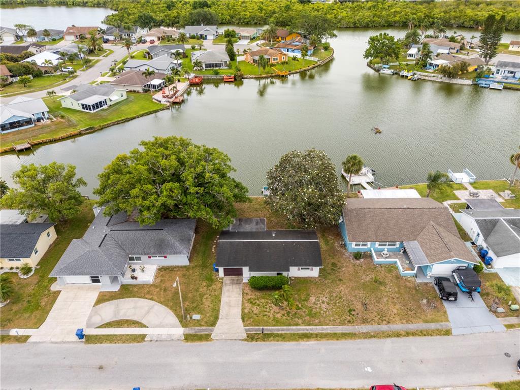 An aerial view shows three suburban houses along a canal with docks and trees — 3510 WILSON DRIVE, HOLIDAY, FL