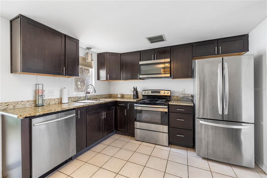 A kitchen features dark wood cabinets, granite countertops, stainless steel appliances, and tiled flooring — 3510 WILSON DRIVE, HOLIDAY, FL