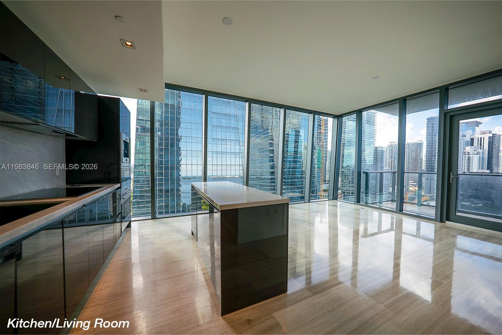 A modern kitchen with dark cabinetry and a central island overlooks a city skyline — 1451 Brickell Ave # 2706, Miami FL 33131, MIAMI, FL