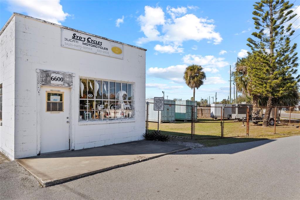 A white, single-story commercial building with a large front window and an adjacent fenced lot — 6600 HAINES ROAD N, ST PETERSBURG, FL