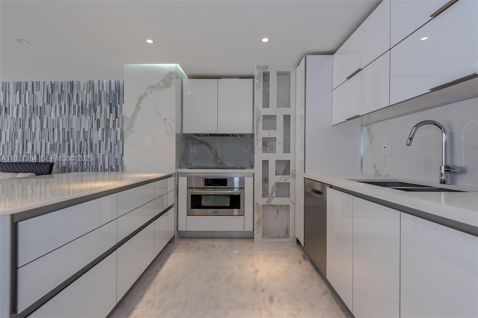 A modern galley kitchen features white high-gloss cabinets, marble countertops, and stainless steel appliances — 6423 Collins Ave # 304, Miami Beach FL 33141, MIAMI BEACH, FL