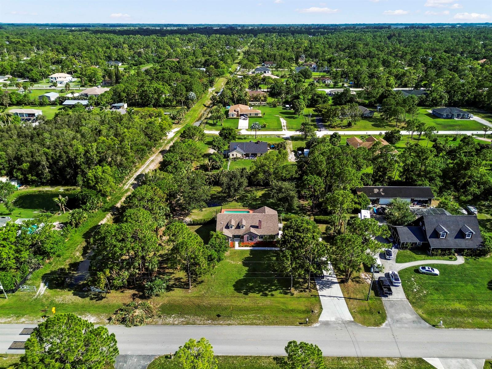 An aerial view shows a residential neighborhood with houses, swimming pools, and dense surrounding trees — 15286 Key Lime Boulevard, Loxahatchee FL 33470, LOXAHATCHEE, FL