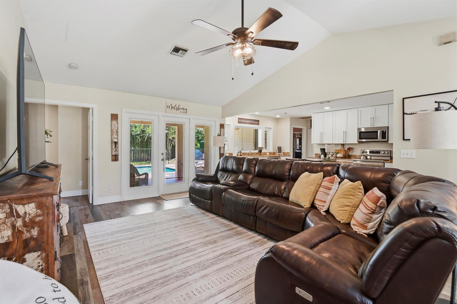 A living room with a brown leather sectional, vaulted ceiling, and views of a backyard pool — 15286 Key Lime Boulevard, Loxahatchee FL 33470, LOXAHATCHEE, FL