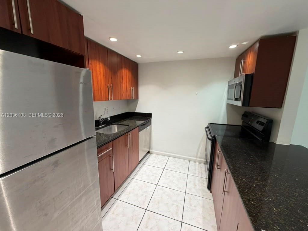 A galley kitchen features dark wood cabinets, black granite countertops, and stainless steel appliances — 1885 NE 121st St # 8, North Miami FL 33181, NORTH MIAMI, FL