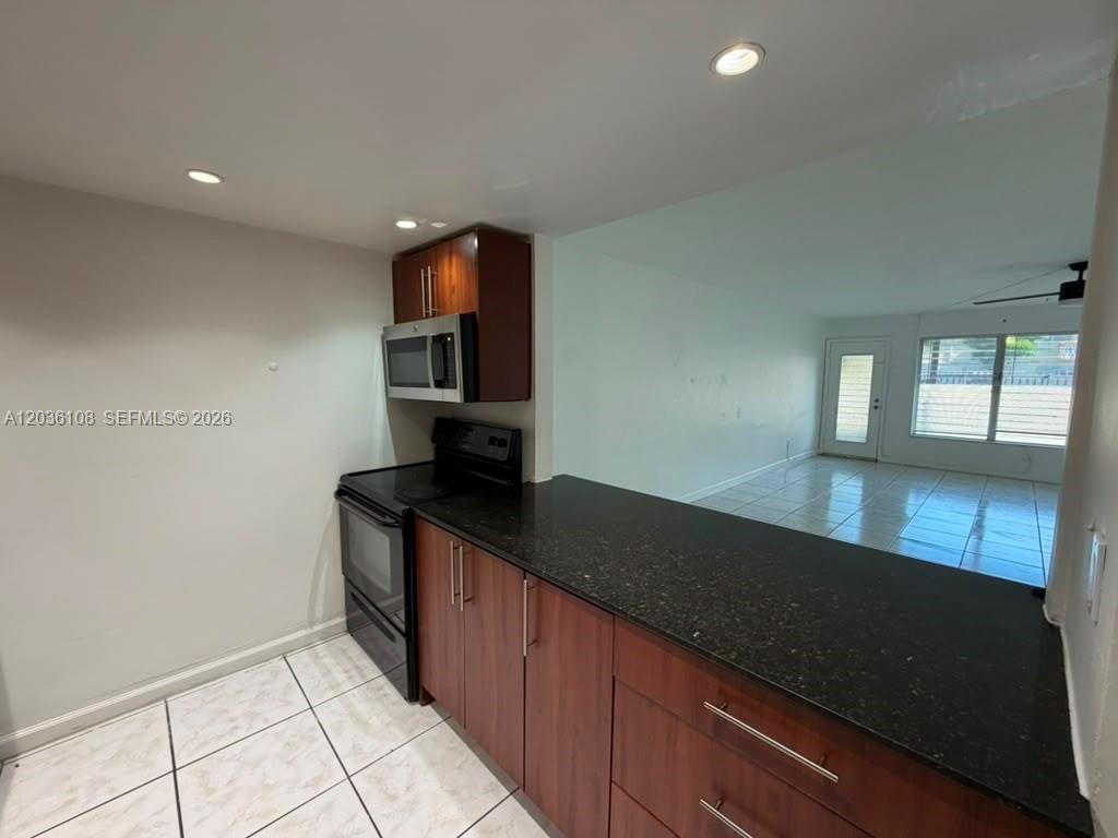 A kitchen features dark wood cabinets, black countertops, and white tile flooring — 1885 NE 121st St # 8, North Miami FL 33181, NORTH MIAMI, FL
