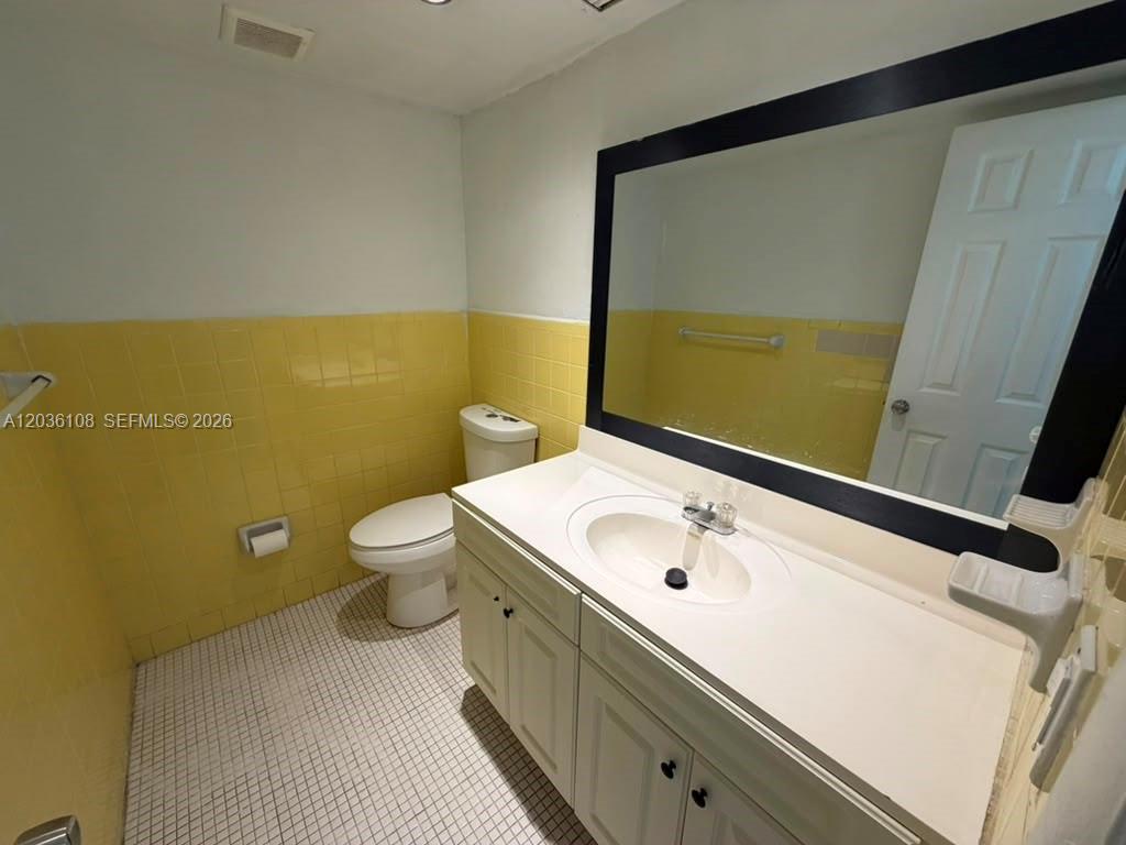 A bathroom features yellow wall tiles, a white vanity, and a large black-framed mirror — 1885 NE 121st St # 8, North Miami FL 33181, NORTH MIAMI, FL