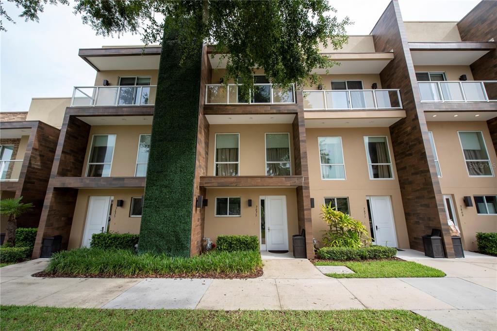 A three-story townhouse exterior features tan stucco walls, wood-look siding, and a vertical green wall — 7673 RECIFE DRIVE, KISSIMMEE, FL