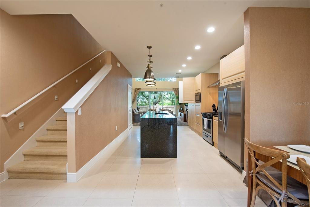 A kitchen with a dark granite island, stainless steel appliances, and stairs leading upstairs — 7673 RECIFE DRIVE, KISSIMMEE, FL