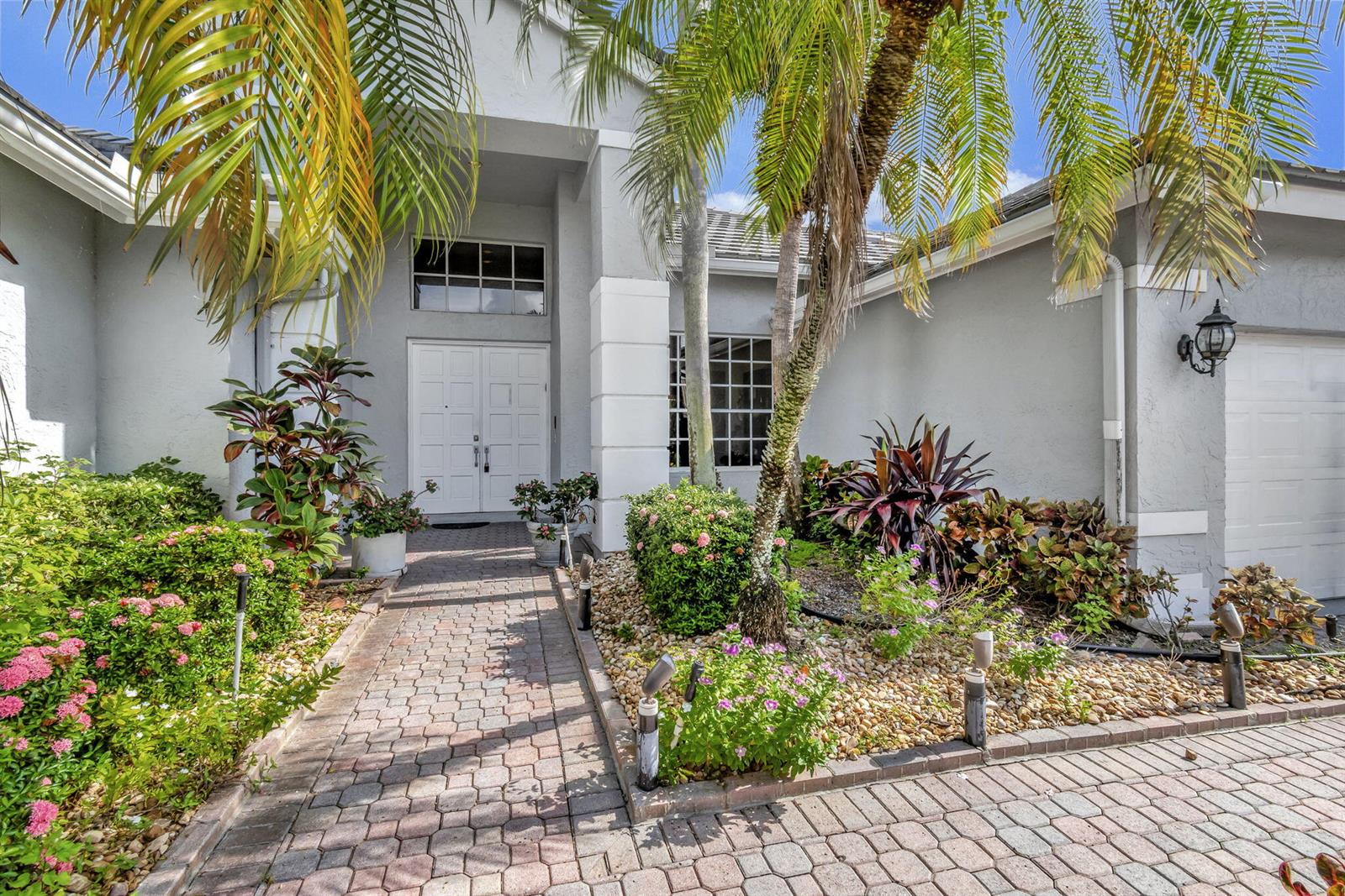 A paved walkway leads to the white double front doors of a grey suburban home — 7791 Bridlington Drive, Boynton Beach FL 33472, BOYNTON BEACH, FL