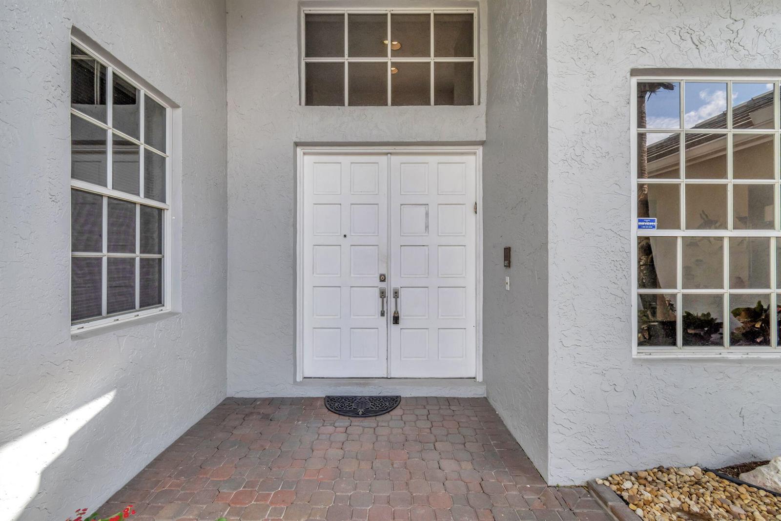 A white double front door with a transom window sits on a brick porch — 7791 Bridlington Drive, Boynton Beach FL 33472, BOYNTON BEACH, FL