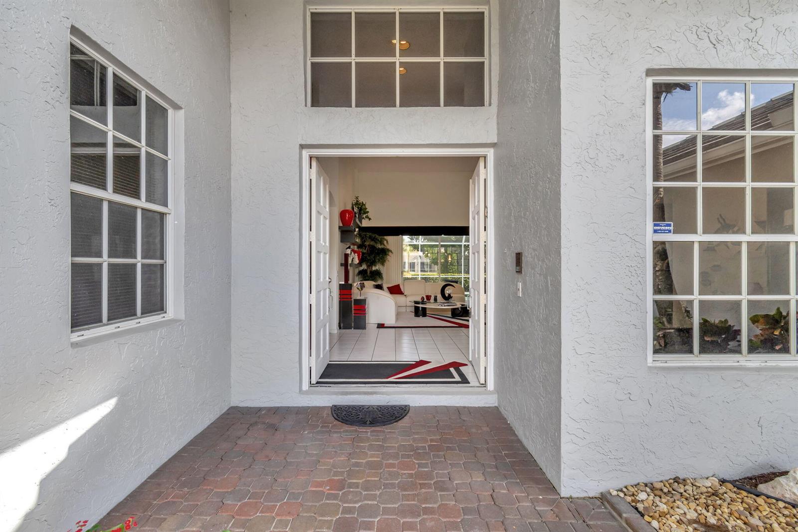 A view from a brick-paved entryway looking through an open doorway into a living room — 7791 Bridlington Drive, Boynton Beach FL 33472, BOYNTON BEACH, FL