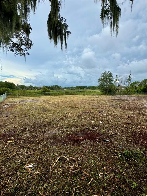 A cleared, grassy lot features a chain-link fence bordering a distant treeline under a cloudy sky — 2713 NEWMARK DRIVE, DELTONA, FL