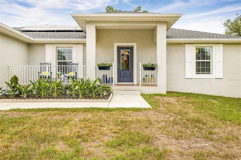 A single-story house exterior features a covered porch, a blue front door, and landscaping — 14330 MAIDSTONE AVENUE, PORT CHARLOTTE, FL