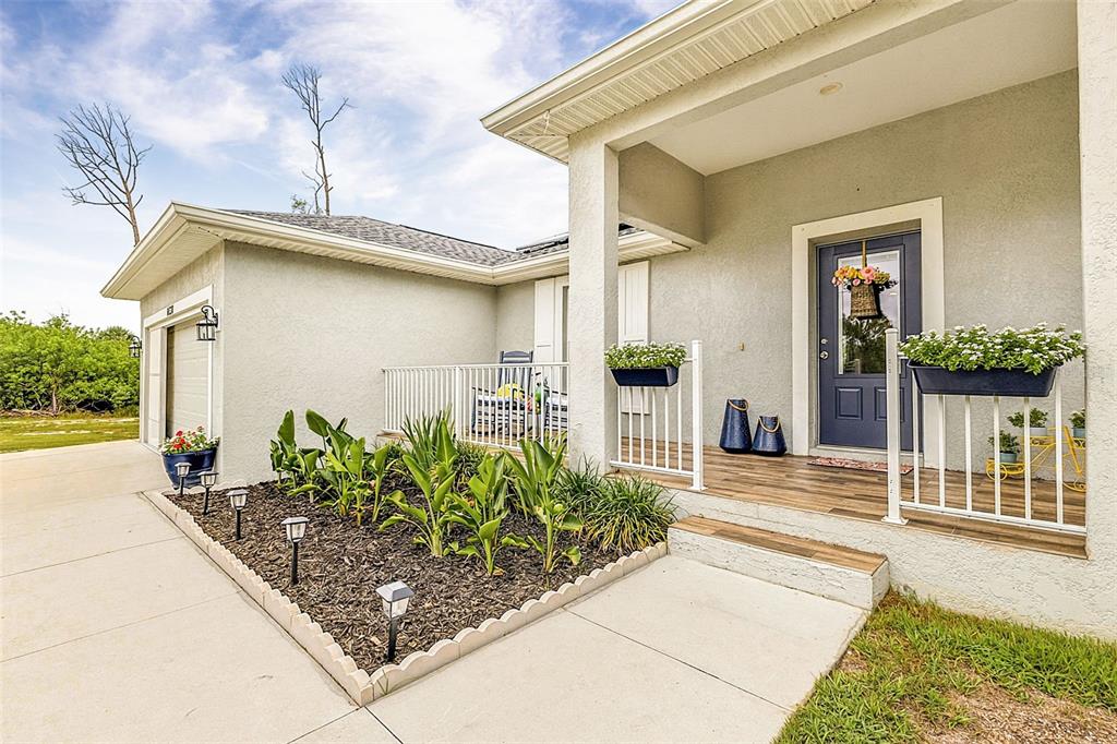 A single-story house exterior features a front porch, a blue door, and a landscaped garden — 14330 MAIDSTONE AVENUE, PORT CHARLOTTE, FL