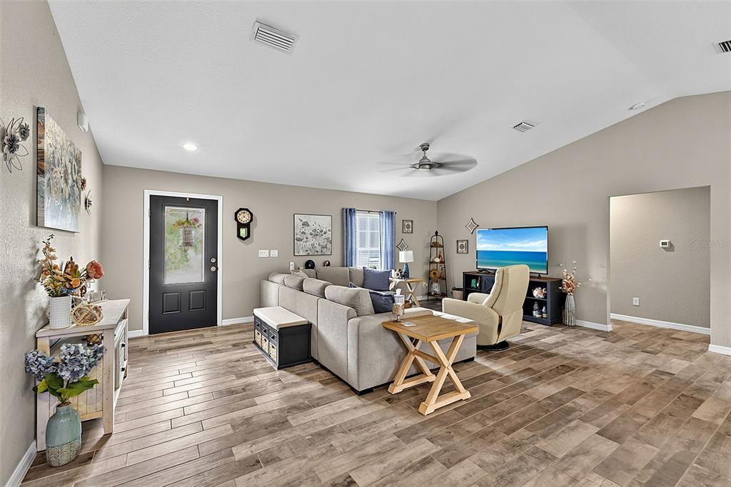 A living room features a grey sectional sofa, wood-look tile flooring, and a vaulted ceiling — 14330 MAIDSTONE AVENUE, PORT CHARLOTTE, FL