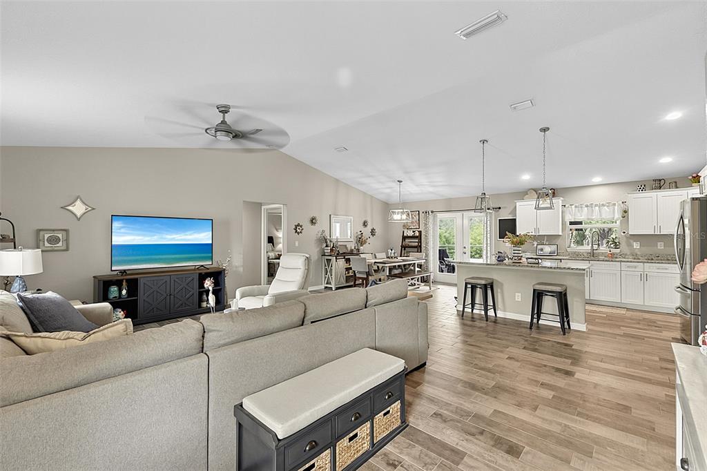 An open-concept living room and kitchen feature light gray walls, wood-look tile flooring, and vaulted ceilings — 14330 MAIDSTONE AVENUE, PORT CHARLOTTE, FL