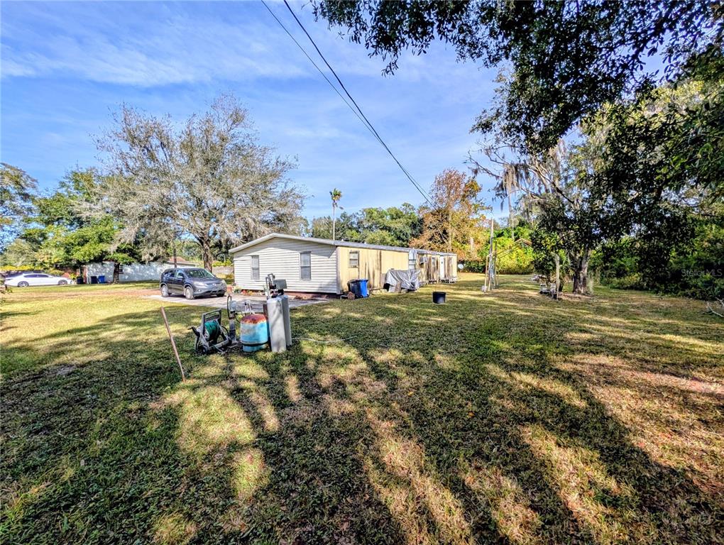 A single-story mobile home sits on a grassy lot with trees and a parked car — 8412 PETERSON ROAD, ODESSA, FL