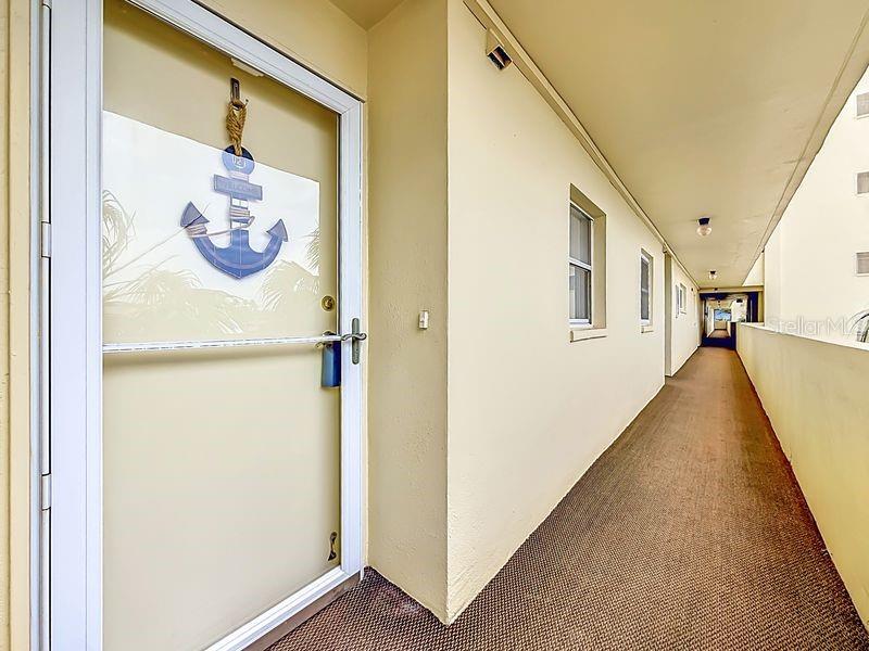 An exterior hallway with a door featuring an anchor decoration leads to a building entrance — 4550 COVE CIRCLE UNIT 302, ST PETERSBURG, FL