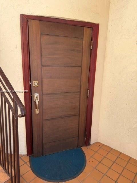 A wooden front door with horizontal panels and a metal handle stands on a tiled porch — 4627 Ponce De Leon Blvd, Coral Gables FL 33146, CORAL GABLES, FL