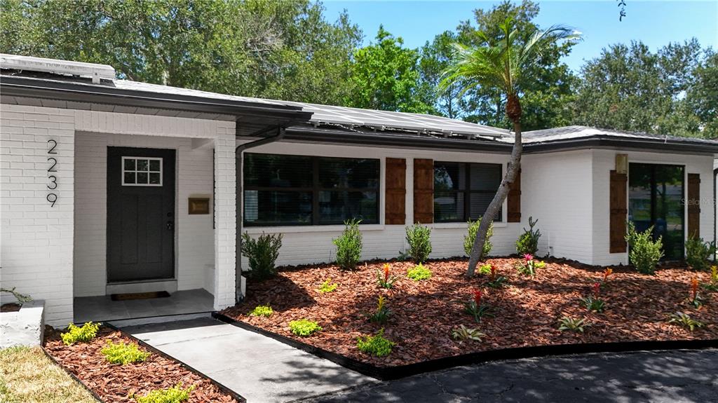 A white brick house exterior features a dark front door, large windows, and landscaped mulch beds — 2239 68TH AVENUE N, ST PETERSBURG, FL