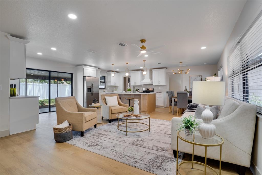 An open-concept living room and kitchen feature light wood floors, white cabinetry, and neutral furniture — 2239 68TH AVENUE N, ST PETERSBURG, FL