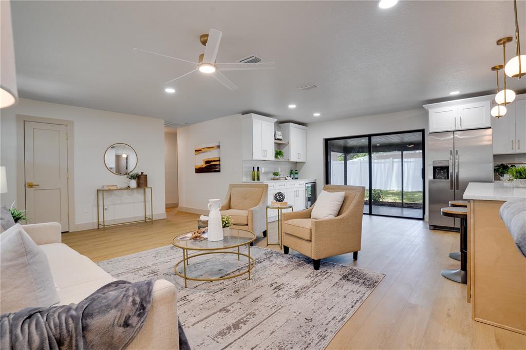 A living room with light wood floors, two armchairs, a sofa, and an open kitchen — 2239 68TH AVENUE N, ST PETERSBURG, FL