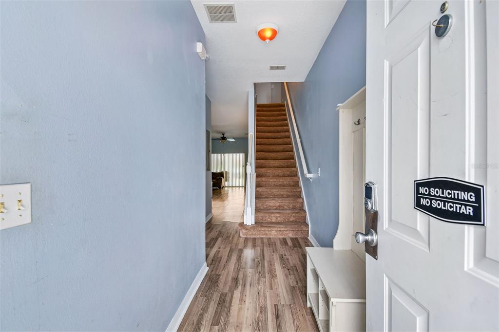 An entryway features wood-look flooring, a carpeted staircase, and a white door with a sign — 1405 RETREAT CIRCLE, CLERMONT, FL