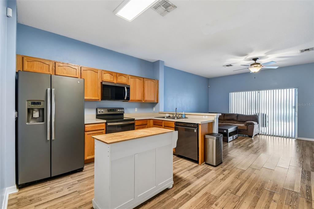 A kitchen with wood cabinets and a white island opens into a living area — 1405 RETREAT CIRCLE, CLERMONT, FL