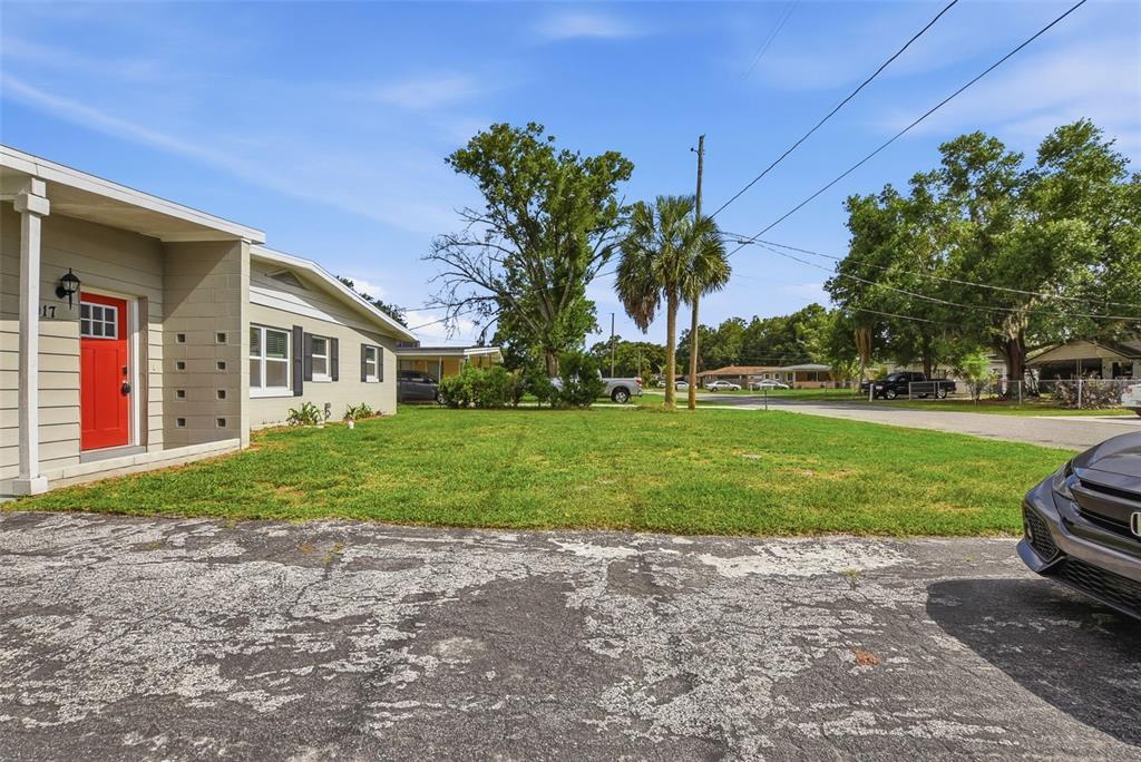 A tan house with a red front door sits beside a large, grassy front yard — 917 KENSINGTON DRIVE, ORLANDO, FL