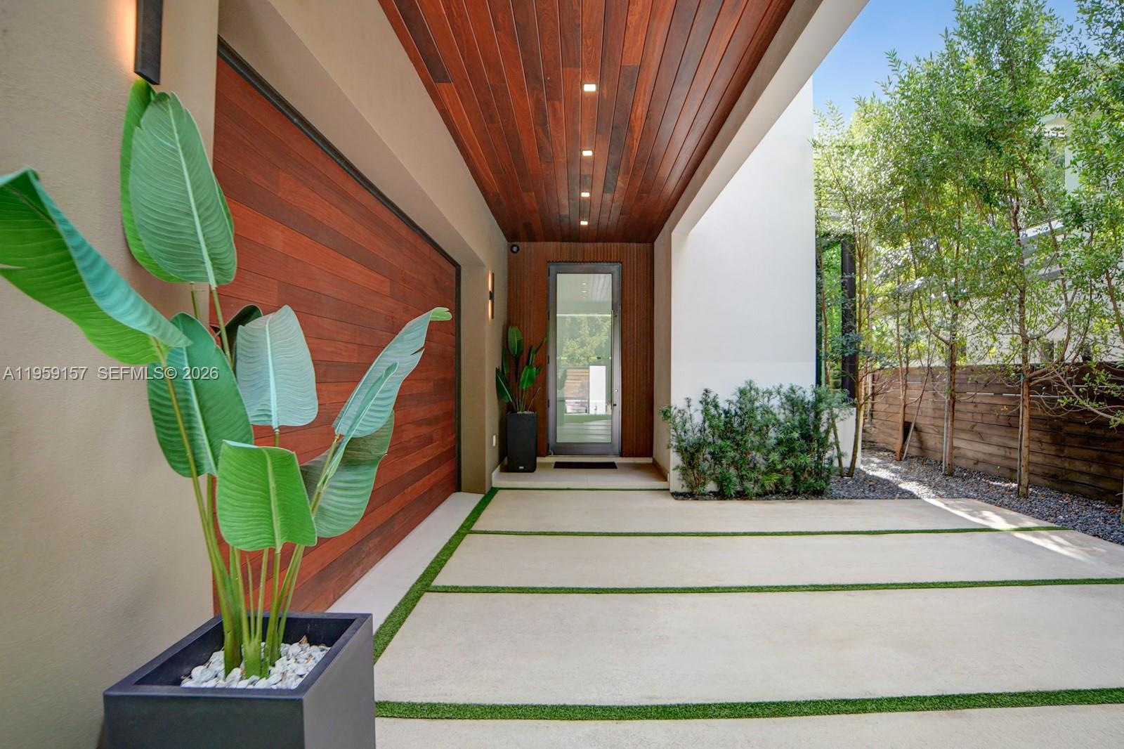 A modern home entrance features a wood-paneled ceiling, a glass door, and a concrete driveway — 1780 Chucunantah Rd, Miami FL 33133, MIAMI, FL