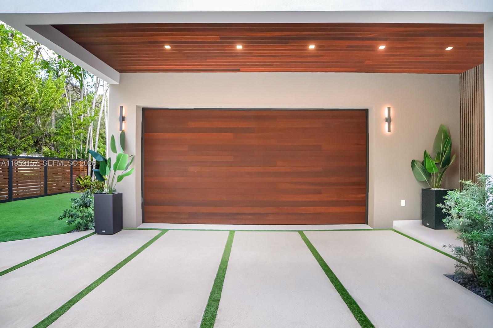 A modern garage features a wood-paneled door, recessed ceiling lights, and a concrete driveway — 1780 Chucunantah Rd, Miami FL 33133, MIAMI, FL